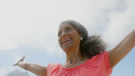 Vista-En-ángulo-Bajo-De-Una-Mujer-Afroamericana-Senior-Activa-Estirando-Sus-Brazos-Bajo-El-Sol-En-La-Playa