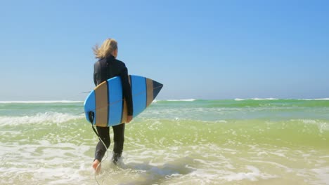 Rear-view-of-active-senior-Caucasian-female-surfer-running-on-sea-in-the-sunshine-4k
