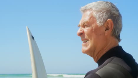 Side-view-of-active-senior-Caucasian-man-standing-with-surfboard-on-the-beach-4k