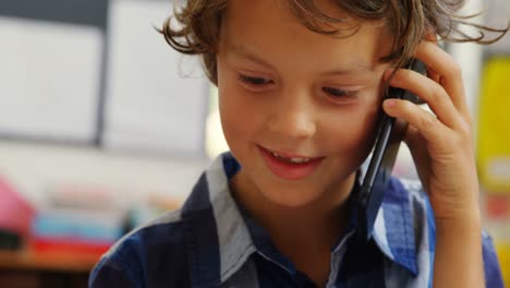 Front-view-of-Caucasian-schoolboy-talking-on-mobile-phone-in-classroom-at-school-4k