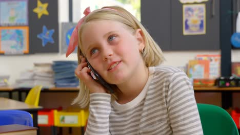 Vorderansicht-Einer-Kaukasischen-Schülerin,-Die-Am-Schreibtisch-Im-Klassenzimmer-Mit-Dem-Mobiltelefon-Spricht,-4K