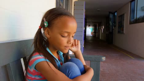 Side-view-of-African-American-schoolgirl-sitting-on-bench-and-crying-in-school-corridor-4k