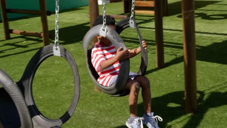 Side-view-of-African-American-schoolboy-playing-on-a-swing-in-school-playground-4k