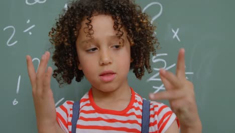 Front-view-of-mixed-race-schoolgirl-counting-with-her-finger-against-chalkboard-in-classroom-4k