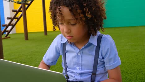 Front-view-of-mixed-race-schoolgirl-studying-on-laptop-in-school-playground-4k