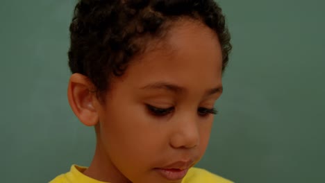 Close-up-of-African-American-schoolboy-standing-against-green-chalkboard-in-classroom-at-school-4k