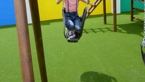 Front-view-of-mixed-race-schoolgirl-playing-on-a-swing-at-school-playground-4k