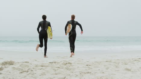 Rückansicht-Von-Zwei-Männlichen-Surfern,-Die-Zusammen-Mit-Einem-Surfbrett-Am-Strand-Laufen,-4k