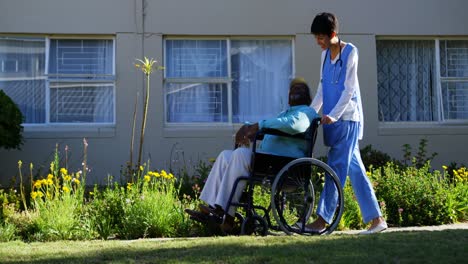 Side-view-of-Caucasian-female-doctor-pushing-senior-patient-in-wheelchair-at-nursing-home-4k
