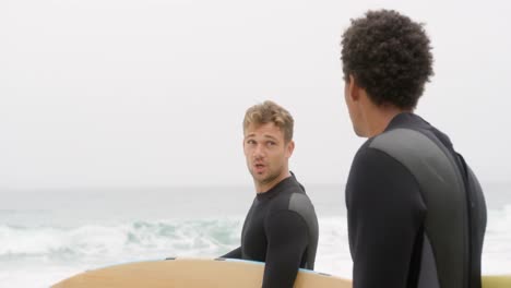 Side-view-of-two-male-surfers-standing-with-surfboard-on-the-beach-4k