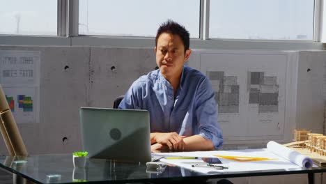 Vorderansicht-Eines-Asiatischen-Männlichen-Architekten-Mit-Laptop-Auf-Dem-Schreibtisch-In-Einem-Modernen-Büro-4K