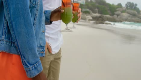 Side-view-of-Mixed-race-couple-holding-cocktail-drink-on-the-beach-4k