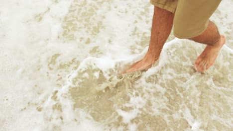 Low-section-of-man-walking-barefoot-on-the-beach-4k