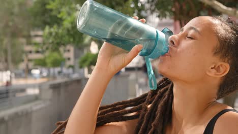 Vista-Lateral-De-Una-Joven-Afroamericana-Bebiendo-Agua-En-La-Ciudad-4k