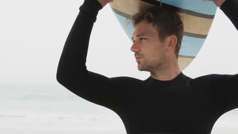Front-view-of-Caucasian-male-surfer-carrying-surfboard-on-his-head-at-beach-4k