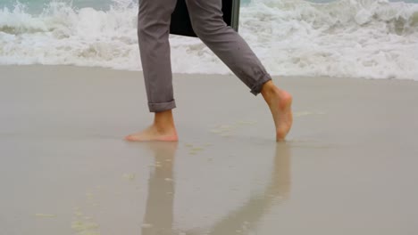 Low-section-of-Businessman-walking-barefoot-with-briefcase-on-the-beach-4k