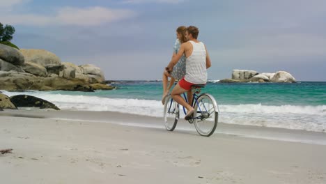 Side-view-of-Caucasian-couple-riding-a-bicycle-on-the-beach-4k