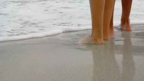 Low-section-of-couple-standing-barefoot-on-the-beach-4k