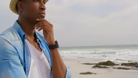 Side-view-of-African-american-man-standing-with-hand-on-chin-at-beach-4k