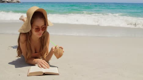 Front-view-of-Caucasian-woman-in-hat-reading-a-book-on-the-beach-4k