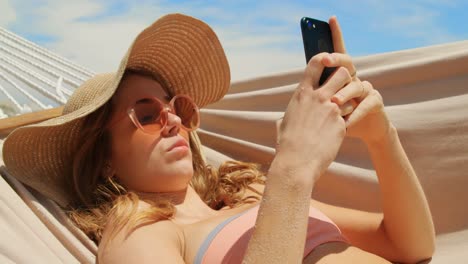 Side-view-of-Caucasian-woman-using-mobile-phone-in-a-hammock-on-the-beach-4k
