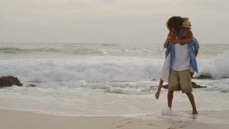 African-american-man-giving-piggyback-ride-to-woman-on-the-beach-4k