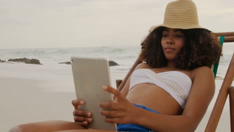 Vista-Frontal-De-Una-Mujer-Afroamericana-Usando-Una-Tableta-Digital-En-La-Playa-4k