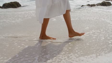 Low-section-of-woman-walking-barefoot-on-a-sunny-day-at-beach-4k