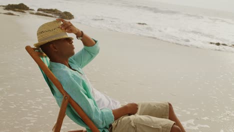 Seitenansicht-Eines-Afroamerikanischen-Mannes,-Der-Sich-In-Einer-Sonnenliege-Am-Strand-Entspannt,-4k