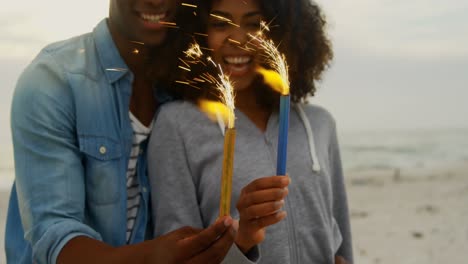 Front-view-of-African-american-couple-holding-sparklers-in-hands-at-beach-4k