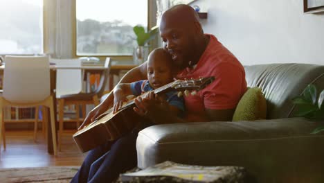 Father-teaching-his-son-how-to-play-guitar-at-home-4k