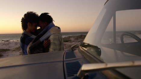 Couple-wrapped-in-blanket-near-pickup-truck-at-beach-during-sunset-4k
