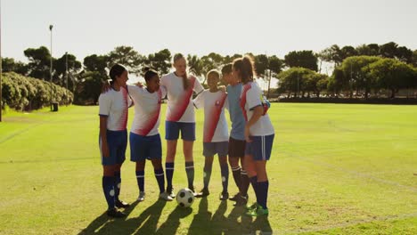 Female-soccer-team-standing-arm-to-arm-on-soccer-field.-4k