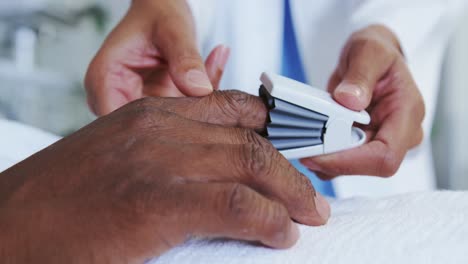 Close-up-of-African-american-female-doctor-attaching-pulse-oximetry-on-male-patient-hand-in-the-ward
