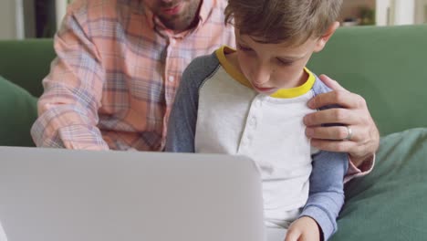 Father-and-son-using-laptop-on-sofa-at-home-4k