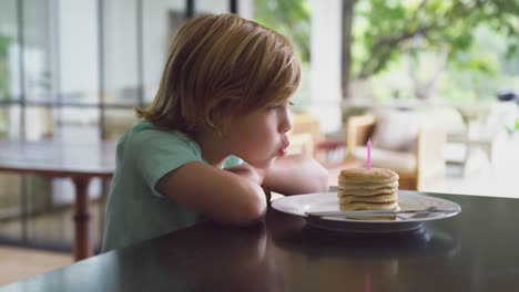 Boy-blowing-candle-on-pancake-at-dining-table-in-kitchen-at-home-4k