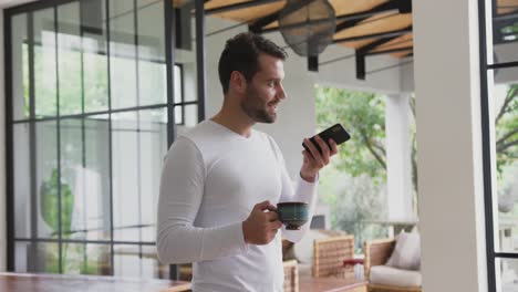 Man-holding-coffee-cup-and-talking-on-mobile-phone-in-a-comfortable-home-4k