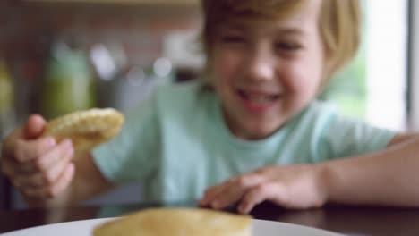 Cute-boy-picking-pancake-from-plate-at-dining-table-in-kitchen-at-home-4k