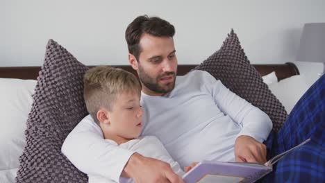 Father-and-son-lying-on-bed-and-reading-a-story-book-in-bedroom-at-home-4k