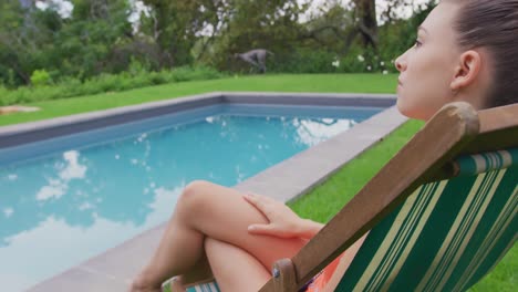 Woman-in-swimwear-relaxing-on-chair-near-swimming-pool-in-the-backyard-4k