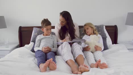 Mother-with-her-children-reading-story-book-in-bedroom-at-home-4k