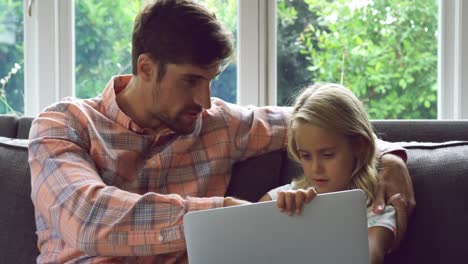 Father-and-daughter-using-laptop-on-sofa-at-home-4k