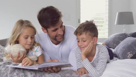 Father-with-his-children-reading-story-book-in-bedroom-at-home-4k