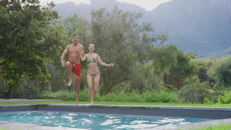 Couple-jumping-together-in-swimming-pool-at-resort-4k