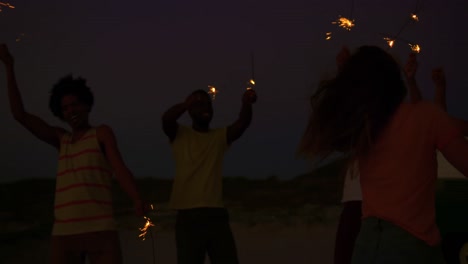 Young-adult-friends-having-fun-on-the-beach-at-night-with-sparklers-4k