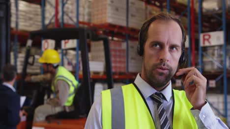 Male-warehouse-manager-using-headset-and-tablet-4k