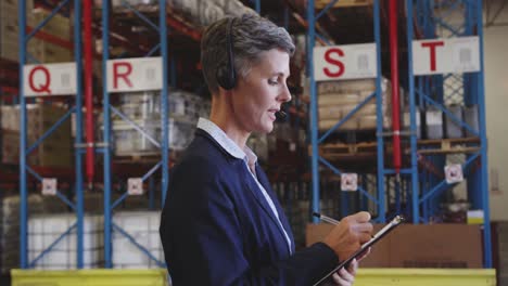 Female-warehouse-manager-talking-with-headset-in-loading-bay-4k