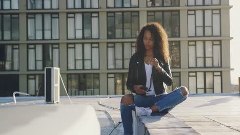 Fashionable-young-woman-on-urban-rooftop-using-smartphone