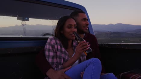 Young-couple-on-a-road-trip-sitting-outside-on-their-truck-at-dusk