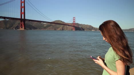 Mujer-Usando-Un-Teléfono-Inteligente-Junto-Al-Puente-Golden-Gate